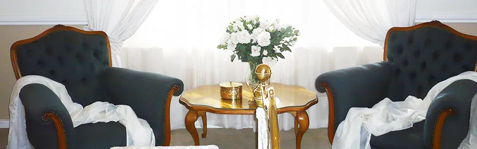 Two dark armchairs with white cloths small table with flowers bright window