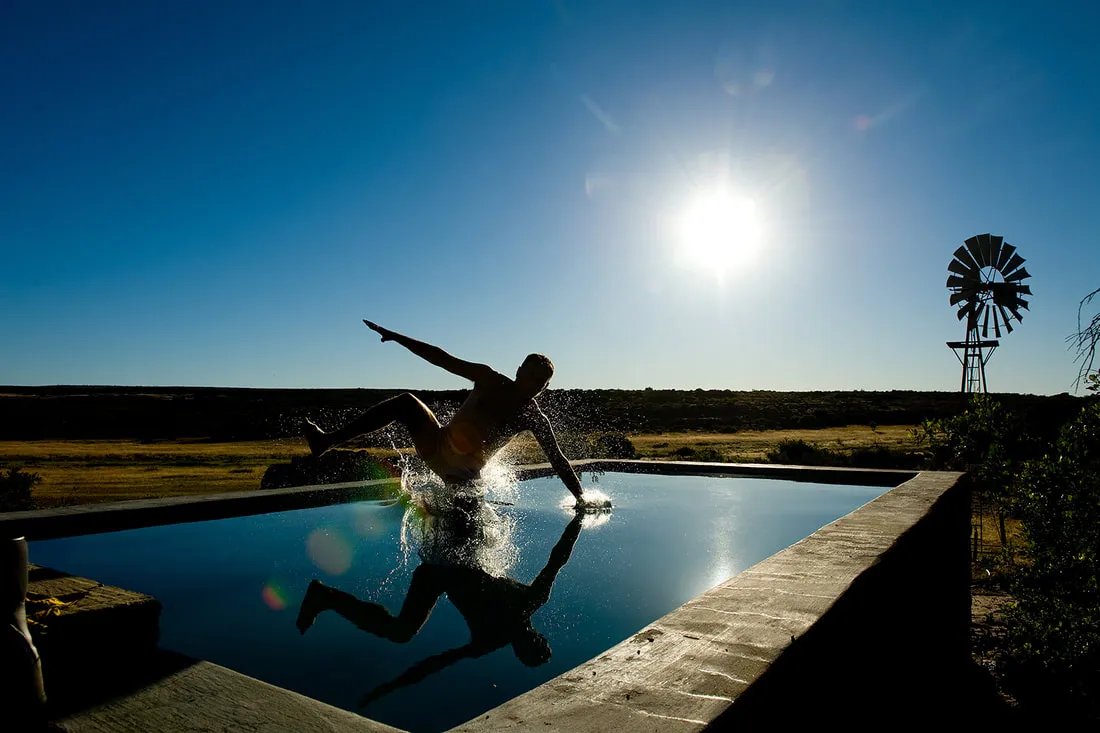 Person jumping into a pool with a windmill in the background under a bright sun