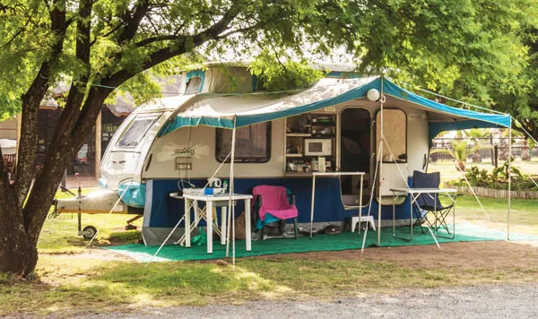 Camper with awning set up in a shaded campsite with outdoor furniture