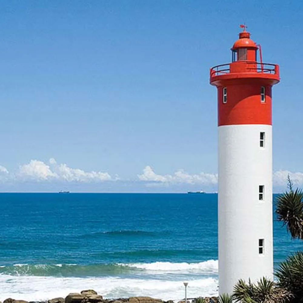 Red and white lighthouse by the ocean with blue sky