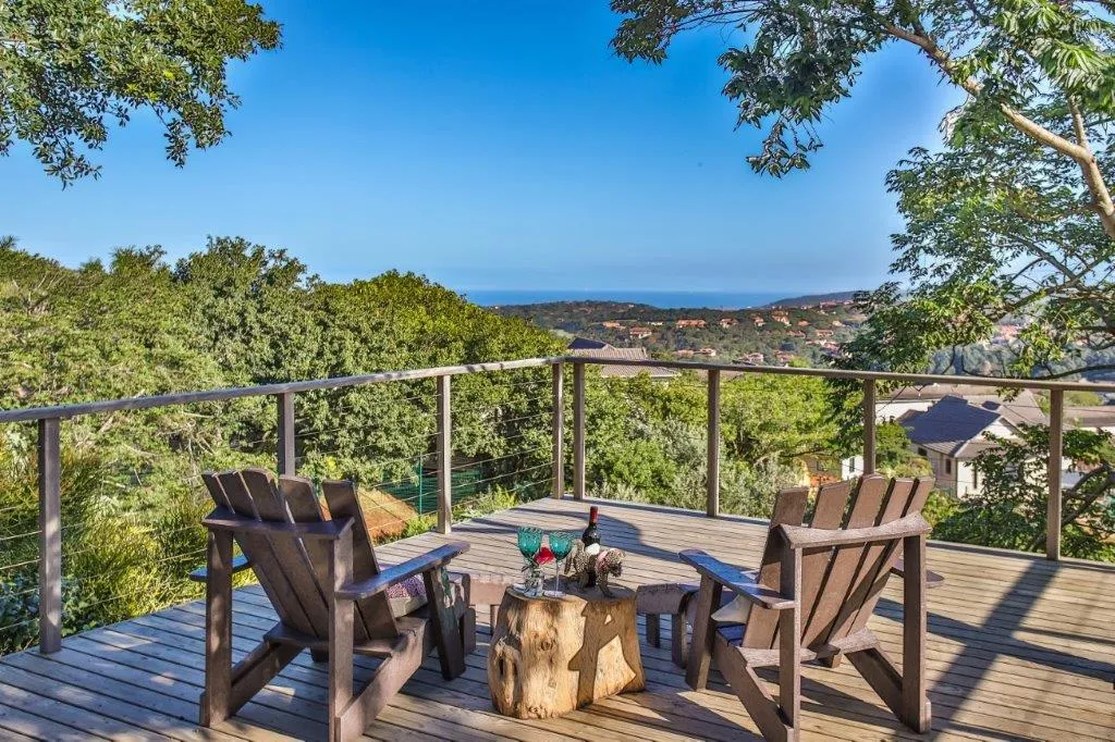 Two wooden chairs on a deck overlooking a scenic landscape with greenery and ocean
