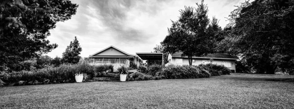 Black and white photo of a house with trees and garden in the foreground