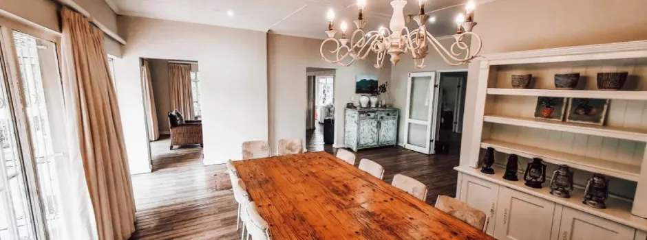 Wooden dining table with chairs in a bright open room with shelves and decor