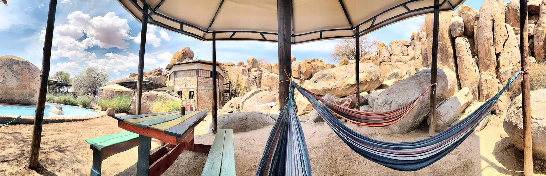 Two hammocks under a canopy with a picnic table and rocky landscape in background
