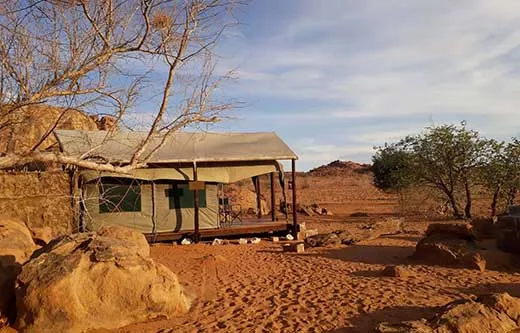Tent cabin in a desert landscape with rocky terrain and sparse vegetation