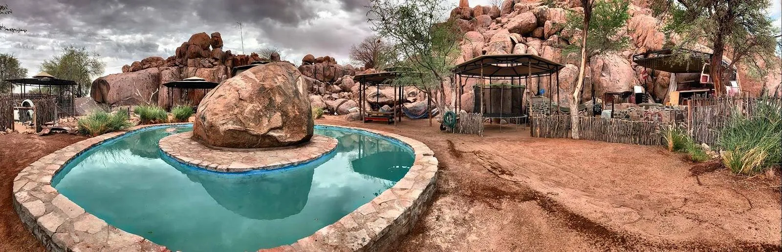 Swimming pool with large rock in desert landscape surrounded by trees and structures