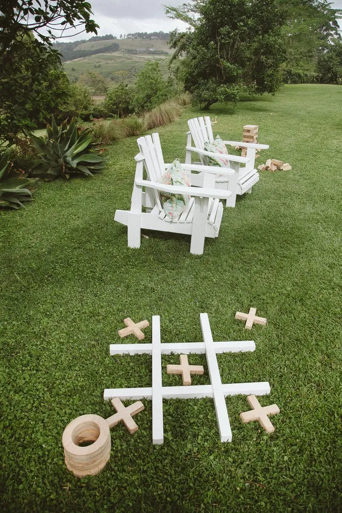 Two white chairs on grass with a large outdoor tictactoe game