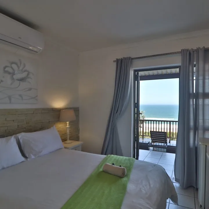 Bedroom with ocean view white bed green throw and sliding glass door