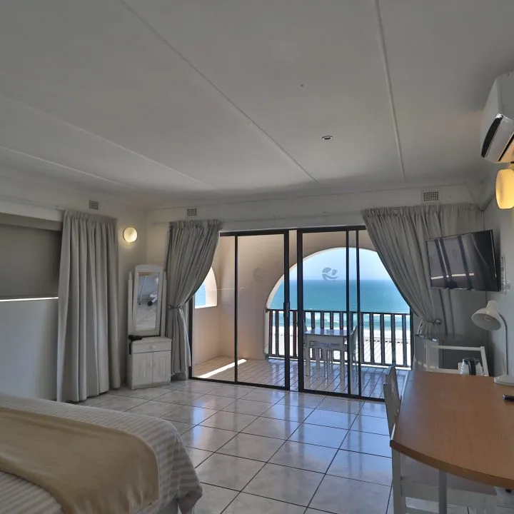 Hotel room with ocean view large windows bed and desk