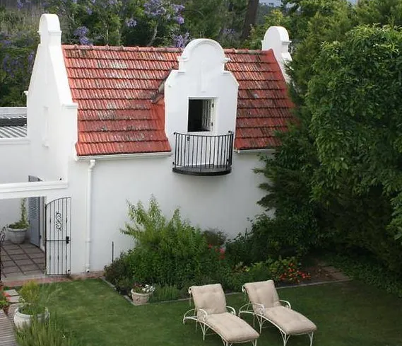 White cottage with redtiled roof surrounded by greenery and two lounge chairs