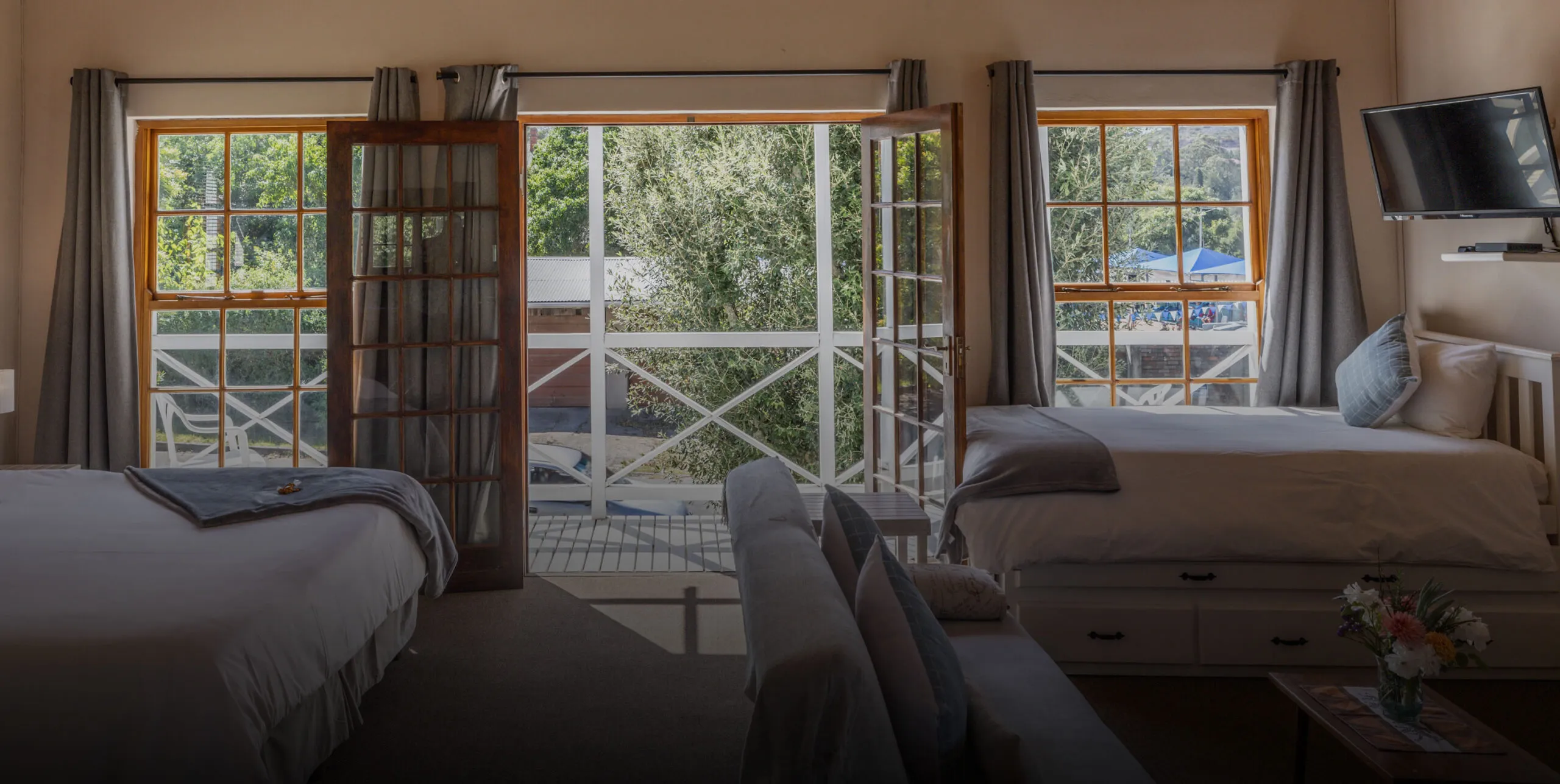 Cozy bedroom with two beds open doors to a balcony and a TV