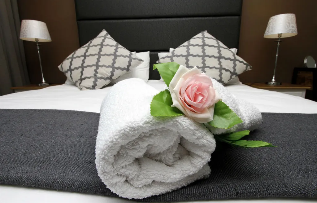 Rolled towel with a rose on a bed with patterned pillows and lamps
