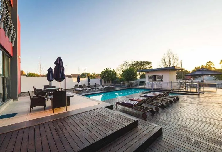Outdoor pool area with lounge chairs umbrellas and a building in the background