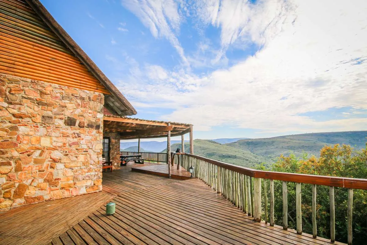 Wooden deck with stone house overlooking a scenic valley with trees and mountains