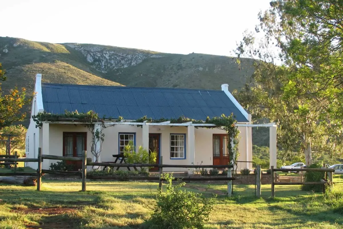 White cottage with a dark roof in a rural setting with mountains in the background