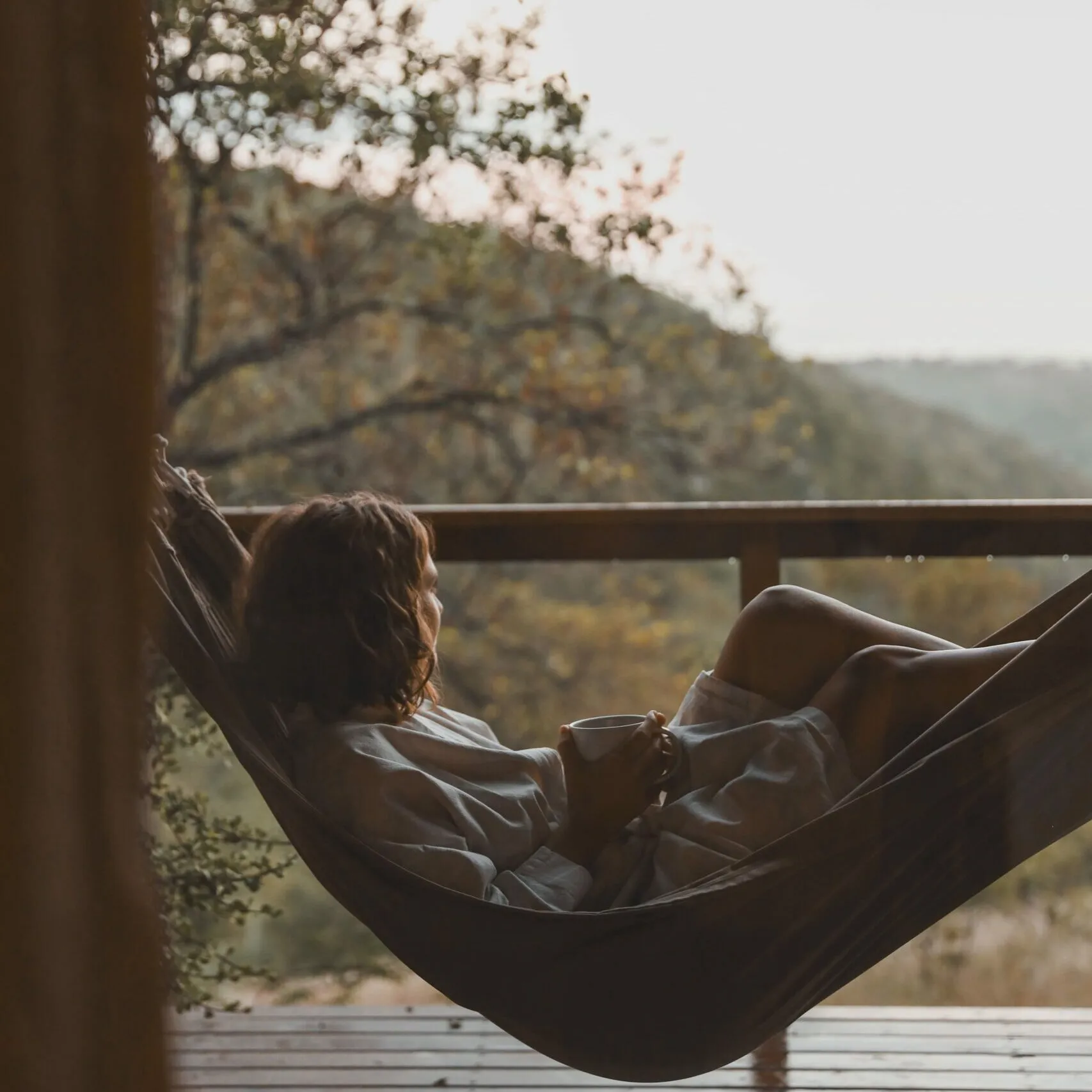 Person relaxing in hammock on wooden deck with scenic forest view