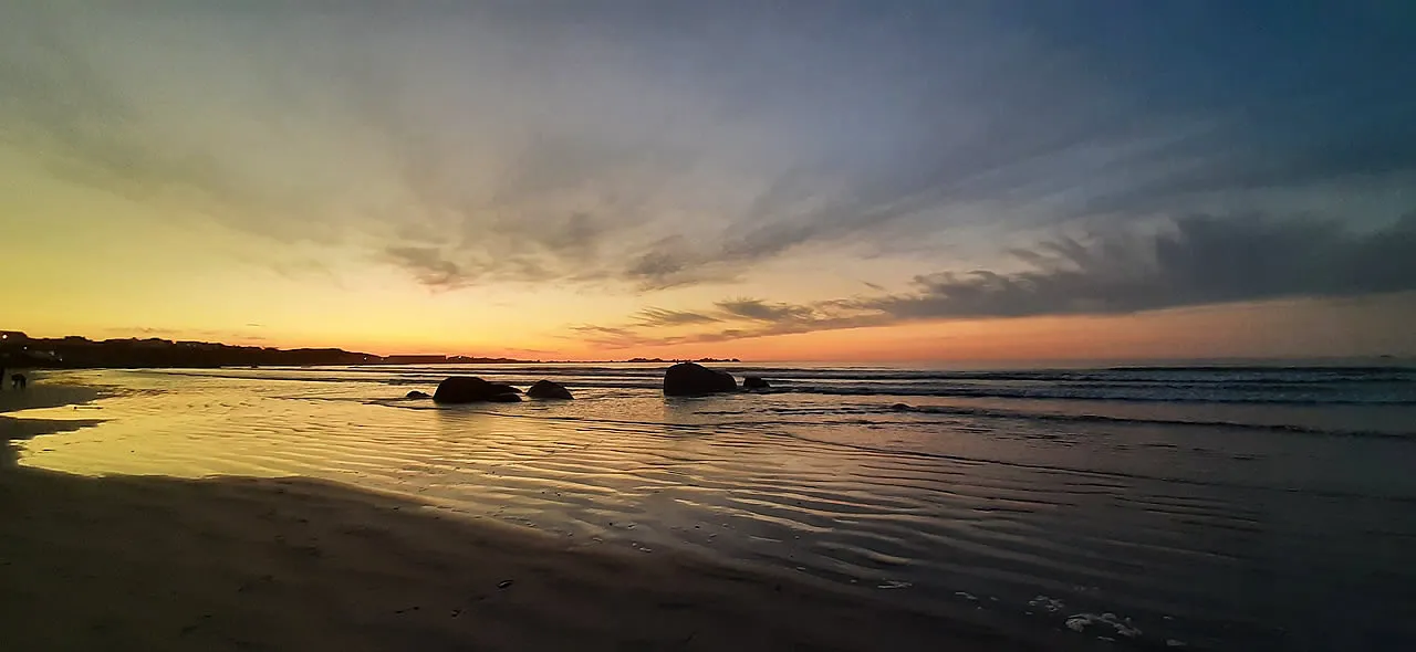 Beach at sunset with rocks in the water and a colorful sky