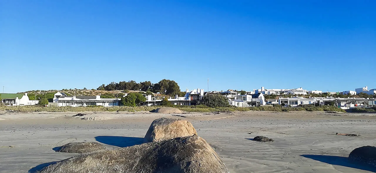 Rocky beach with houses and greenery under a clear blue sky