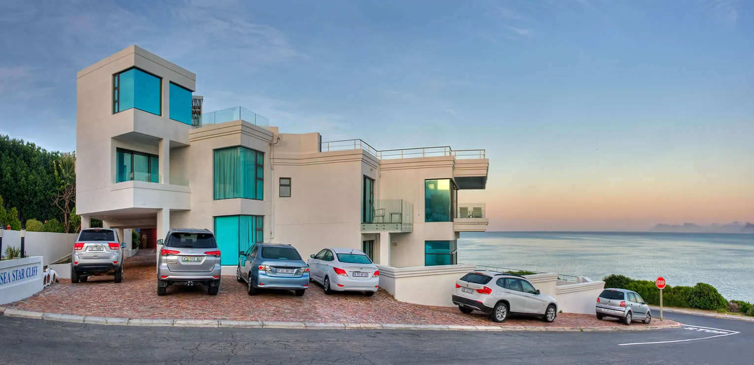 Modern house with multiple cars parked in front overlooking the ocean at sunset