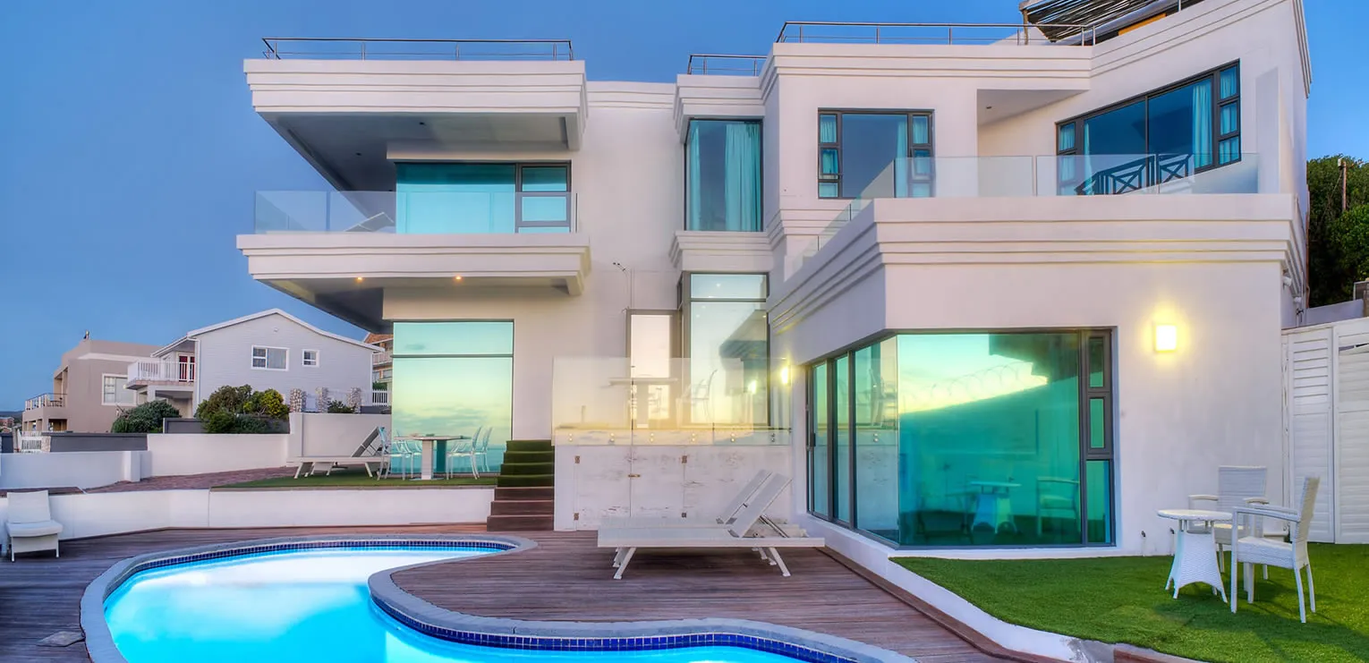 Modern white house with large windows pool and outdoor seating at dusk