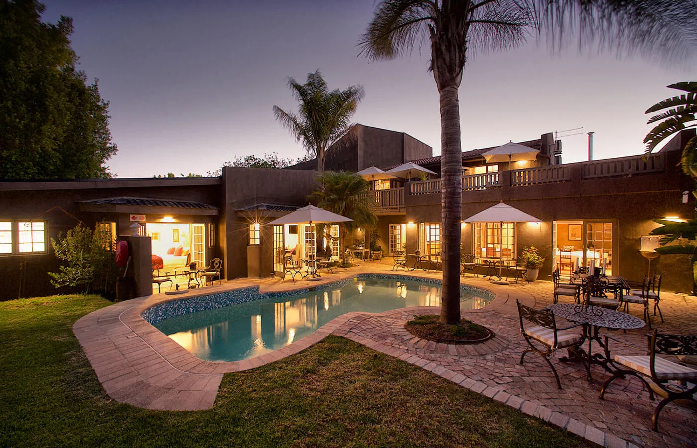 Evening view of a house with a lit pool palm trees and outdoor seating