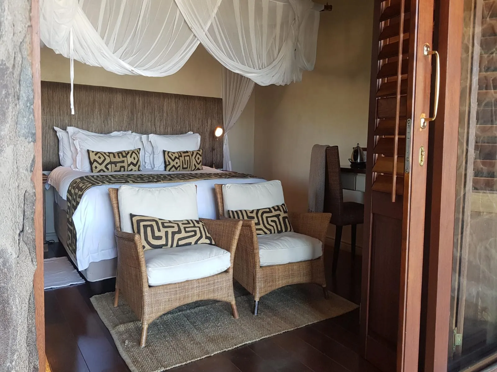 Cozy bedroom with two wicker chairs bed and wooden door to balcony