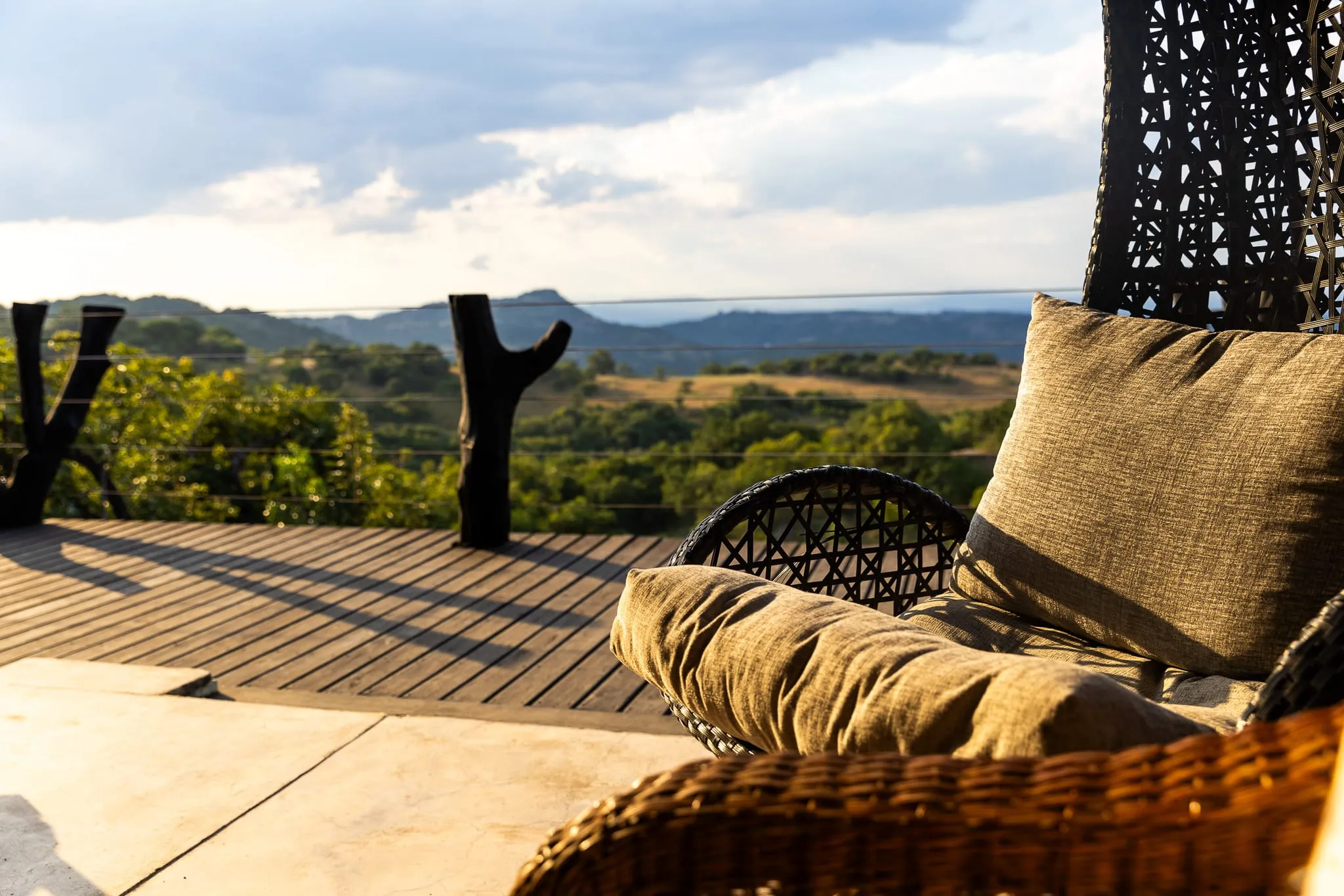 Wooden deck with wicker chair overlooking a scenic landscape with trees and hills