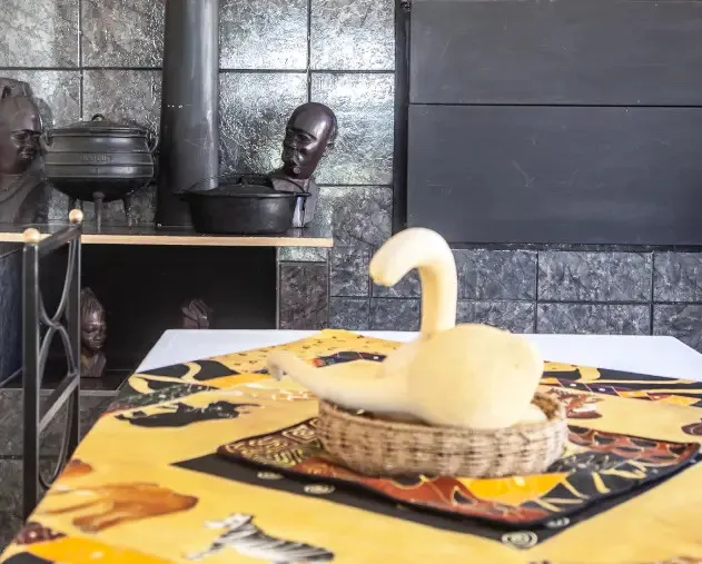 Wooden swan sculpture on a patterned tablecloth in a rustic room with pottery