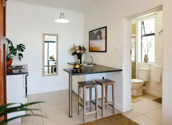 Small kitchenette with bar stools adjacent to a bathroom with toilet and sink