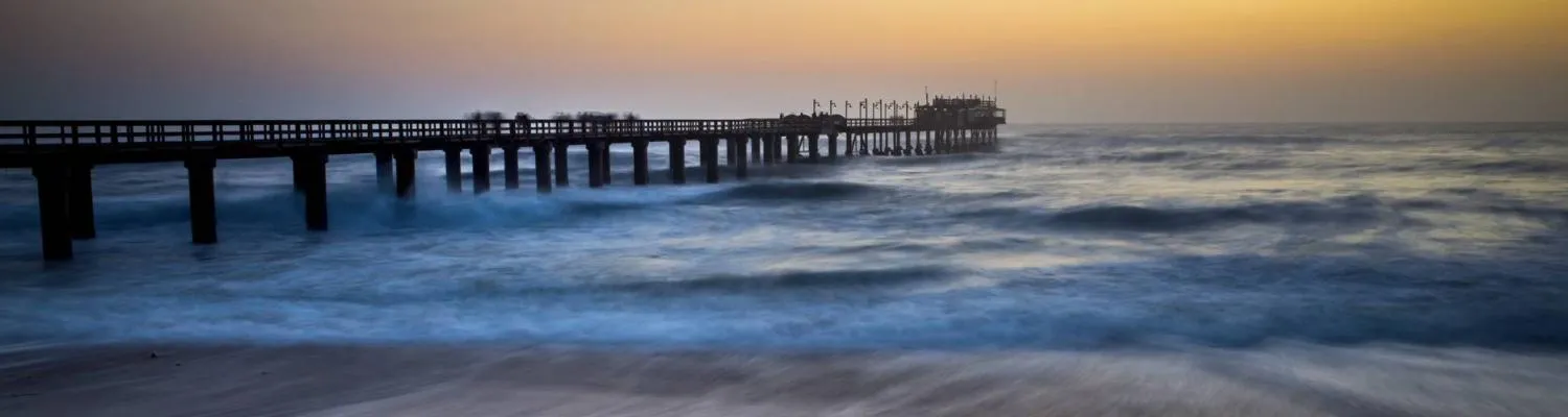Wooden pier extending over ocean waves at sunset with a clear sky