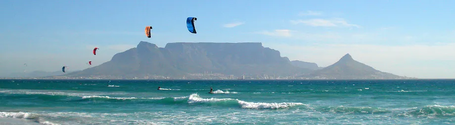 People kite surfing in the ocean with mountains in the background