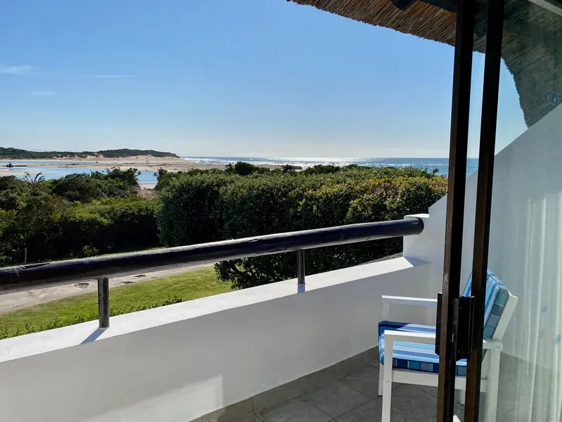 Balcony with blue chair overlooking beach and greenery under clear sky