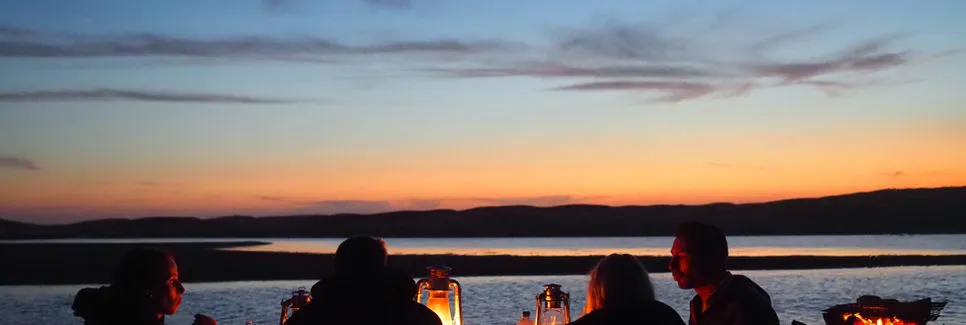 Four people sitting by a lake at sunset with a lantern in the foreground