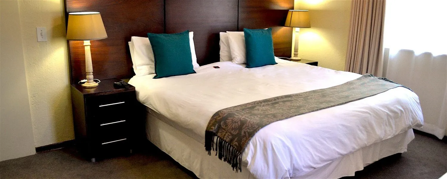 Neatly made bed with white linens teal pillows and bedside lamps in a bedroom