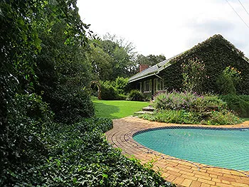 A house with a garden and a swimming pool surrounded by greenery