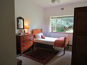 Cozy bedroom with wooden furniture single bed and window view of greenery