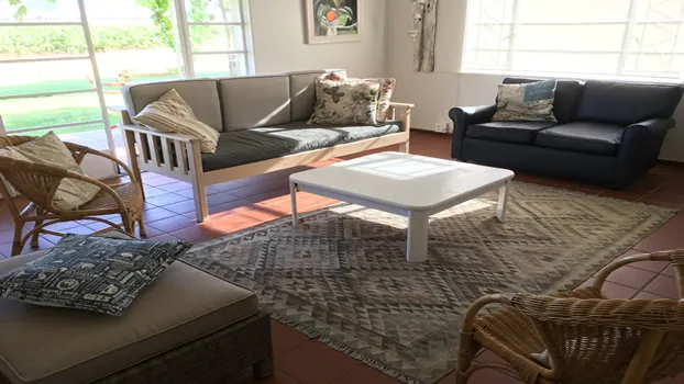 Sunlit living room with various seating options and a patterned rug on tiled floor