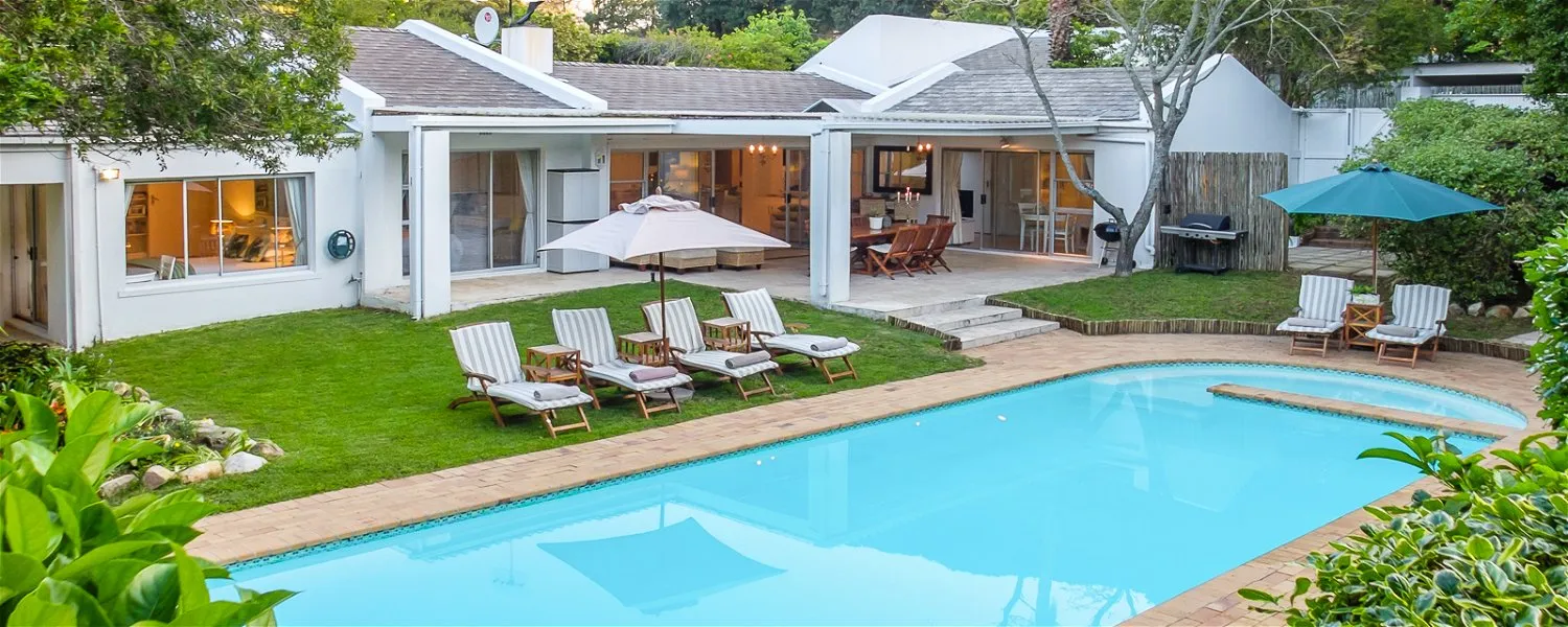 Modern house with pool lounge chairs and umbrellas in a lush garden