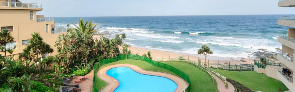 Beachfront view with swimming pool palm trees and ocean waves