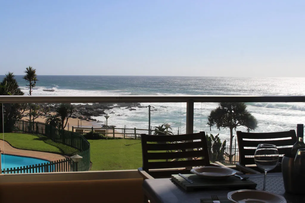 Ocean view from a balcony with dining setup and swimming pool in foreground