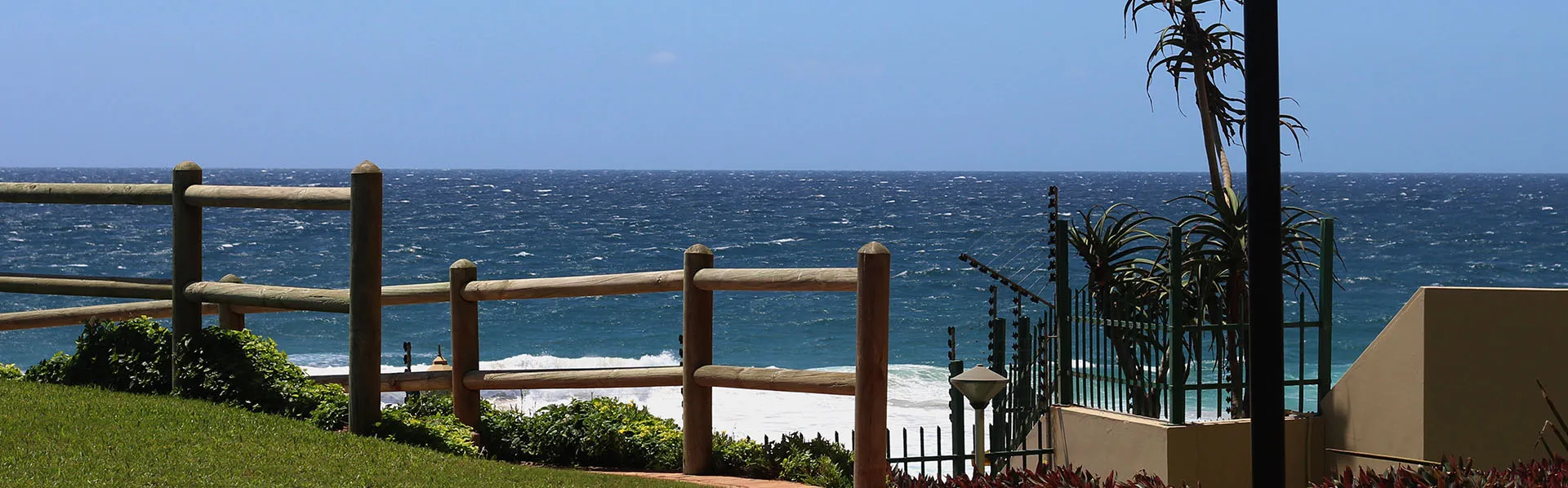 Wooden fence overlooking the ocean with palm trees and a building