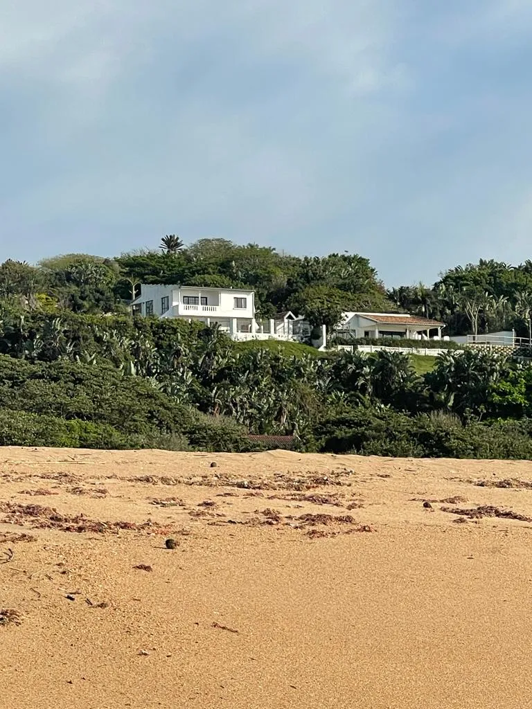 House on a hill overlooking a sandy beach with lush greenery