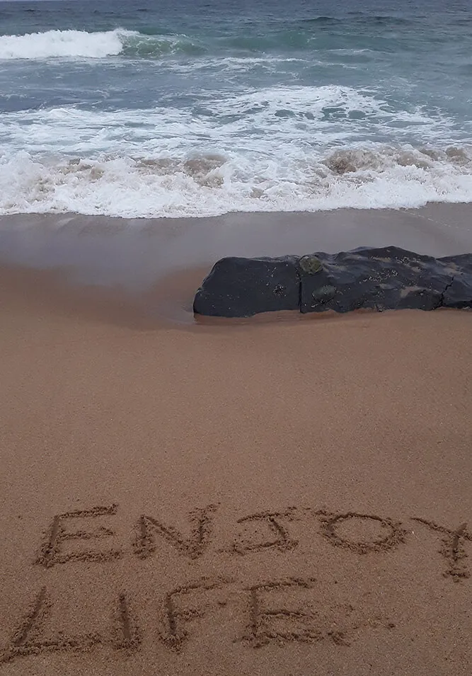 Beach with waves rocks and ENJOY LIFE written in the sand