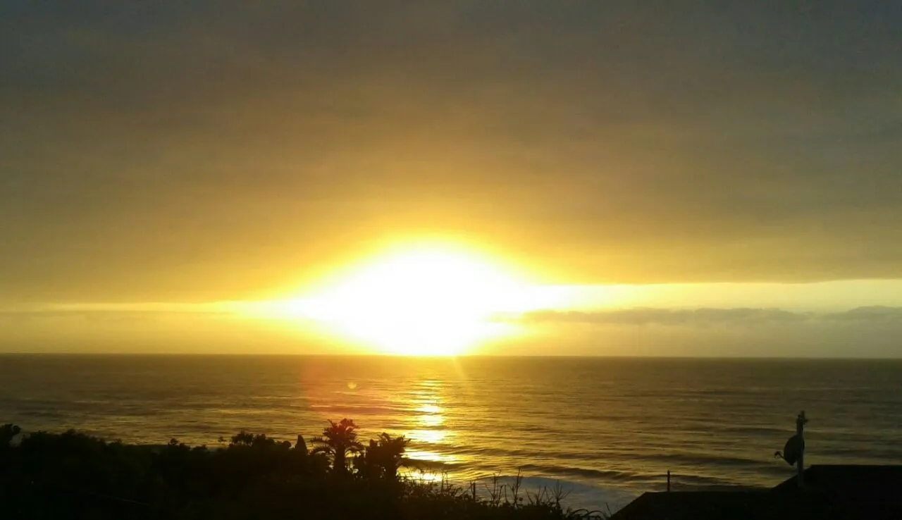 Sunset over the ocean with silhouetted trees and a building in the foreground