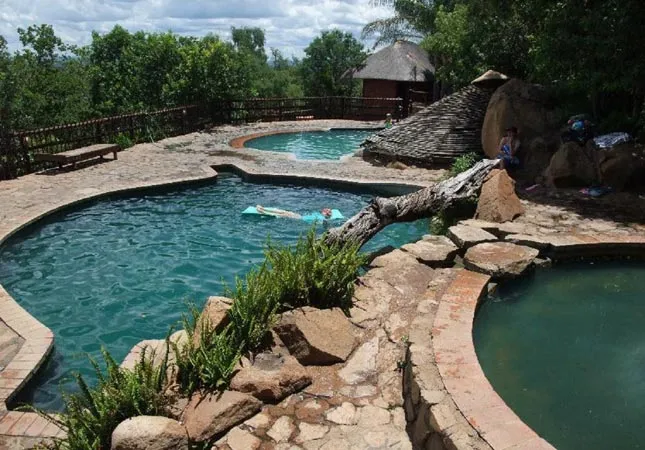 Outdoor hot spring pools with person floating in one surrounded by greenery and rocks