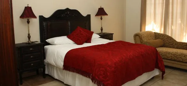 Bedroom with a large bed red blanket and a beige chaise lounge