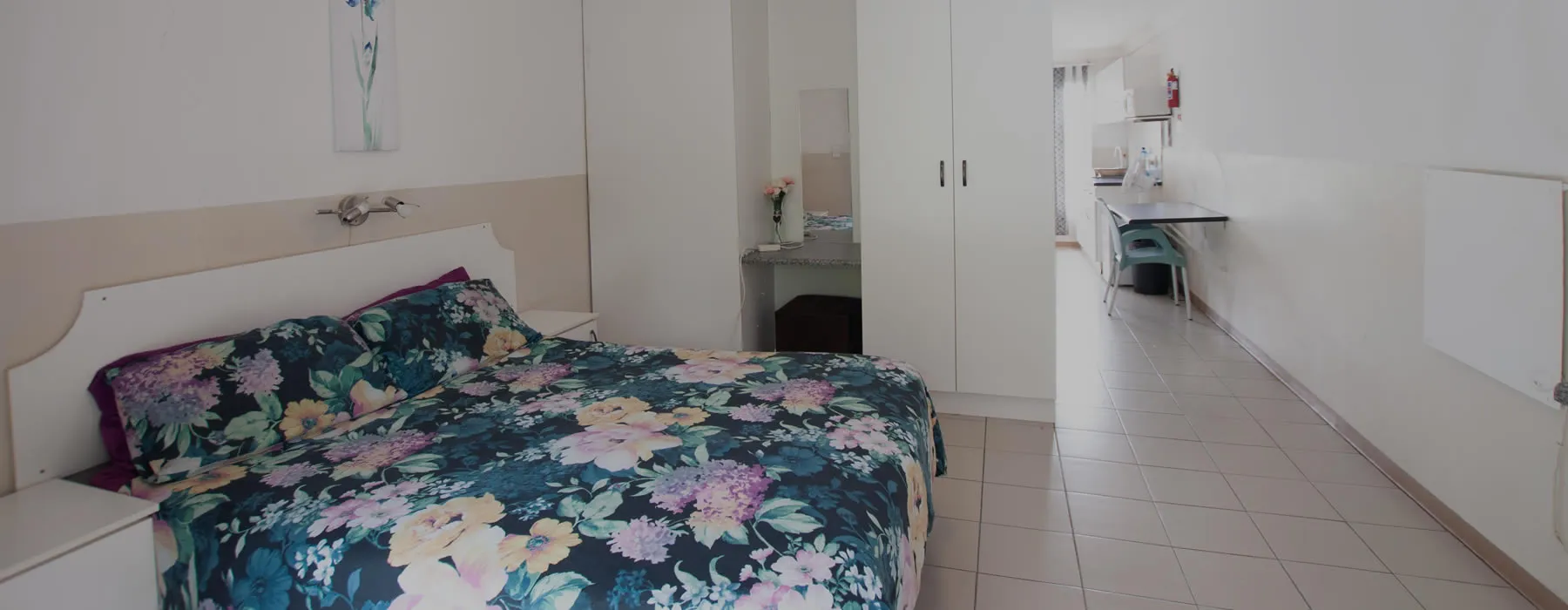 Bedroom with floral bedspread white walls and a hallway leading to another room