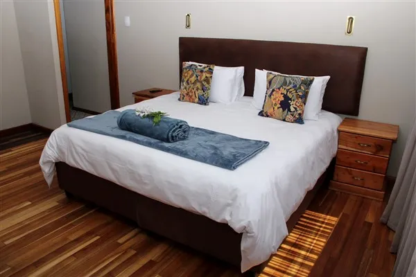 Neatly made bed with colorful pillows and a rolled towel on a blue blanket