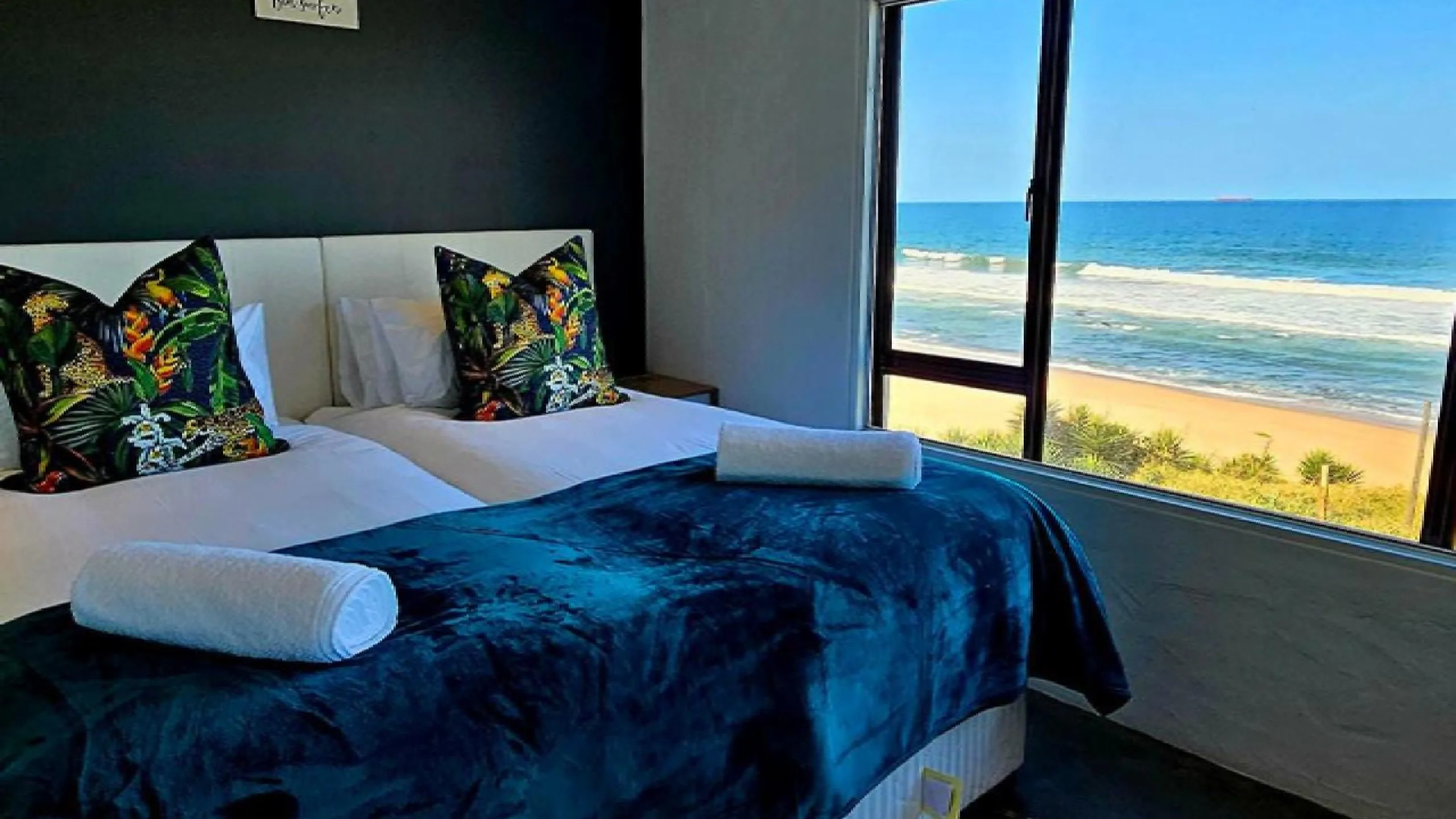 Bedroom with ocean view two beds with blue blanket and tropical pillows