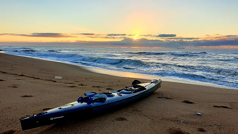 Kayak on a sandy beach at sunset with gentle waves in the background